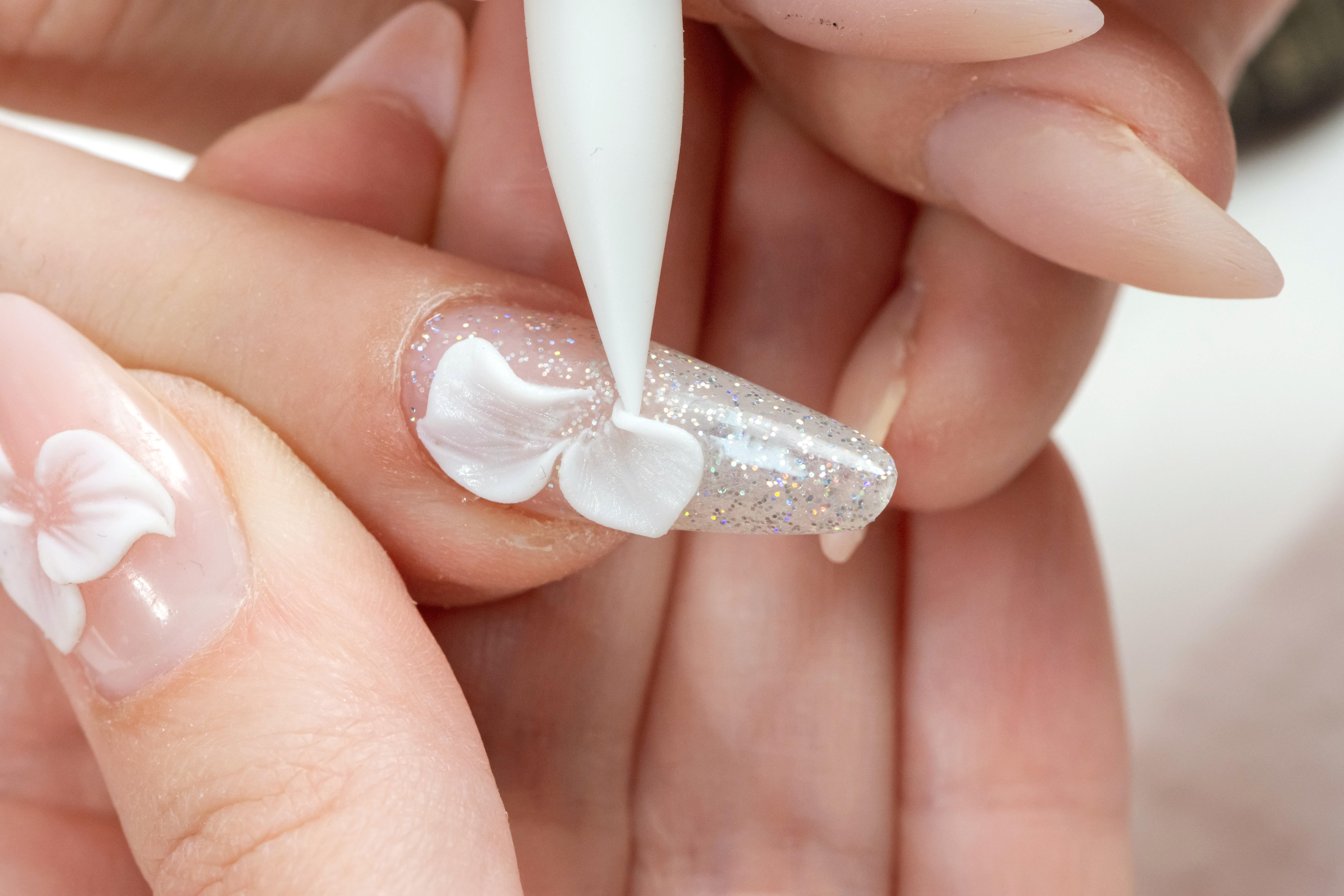 白い花の3Dネイルを施すネイリストの手元