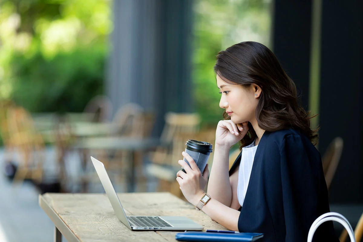 コーヒーを飲みながらパソコンの前で考え事をしている社会人の女性