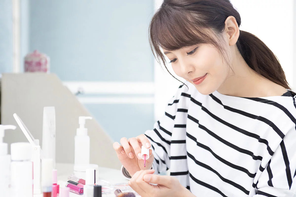 ピンクのマニキュアでセルフネイルをしている女性
